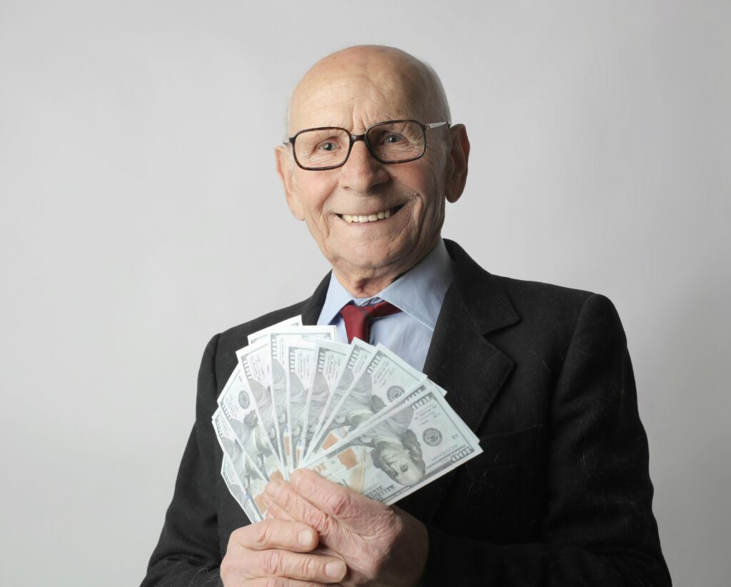 pexels-photo-3831181-3831181 Senior man in a suit with glasses holding US dollars, symbolizing wealth and savings.