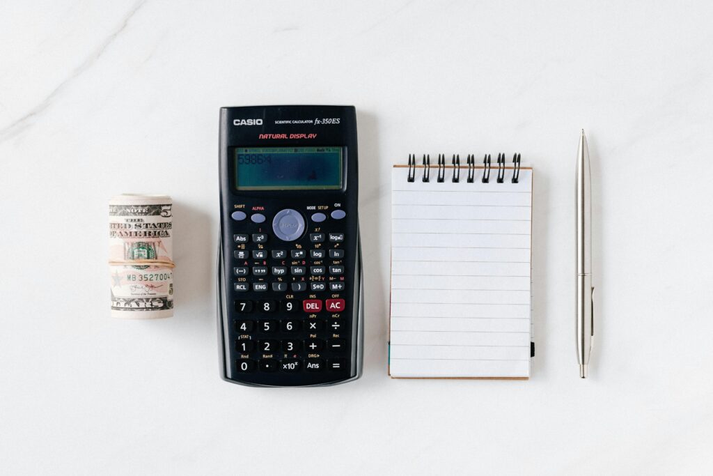 pexels-photo-4386341-4386341 Top view of financial tools including a calculator, notepad, pen, and rolled cash on a white background.